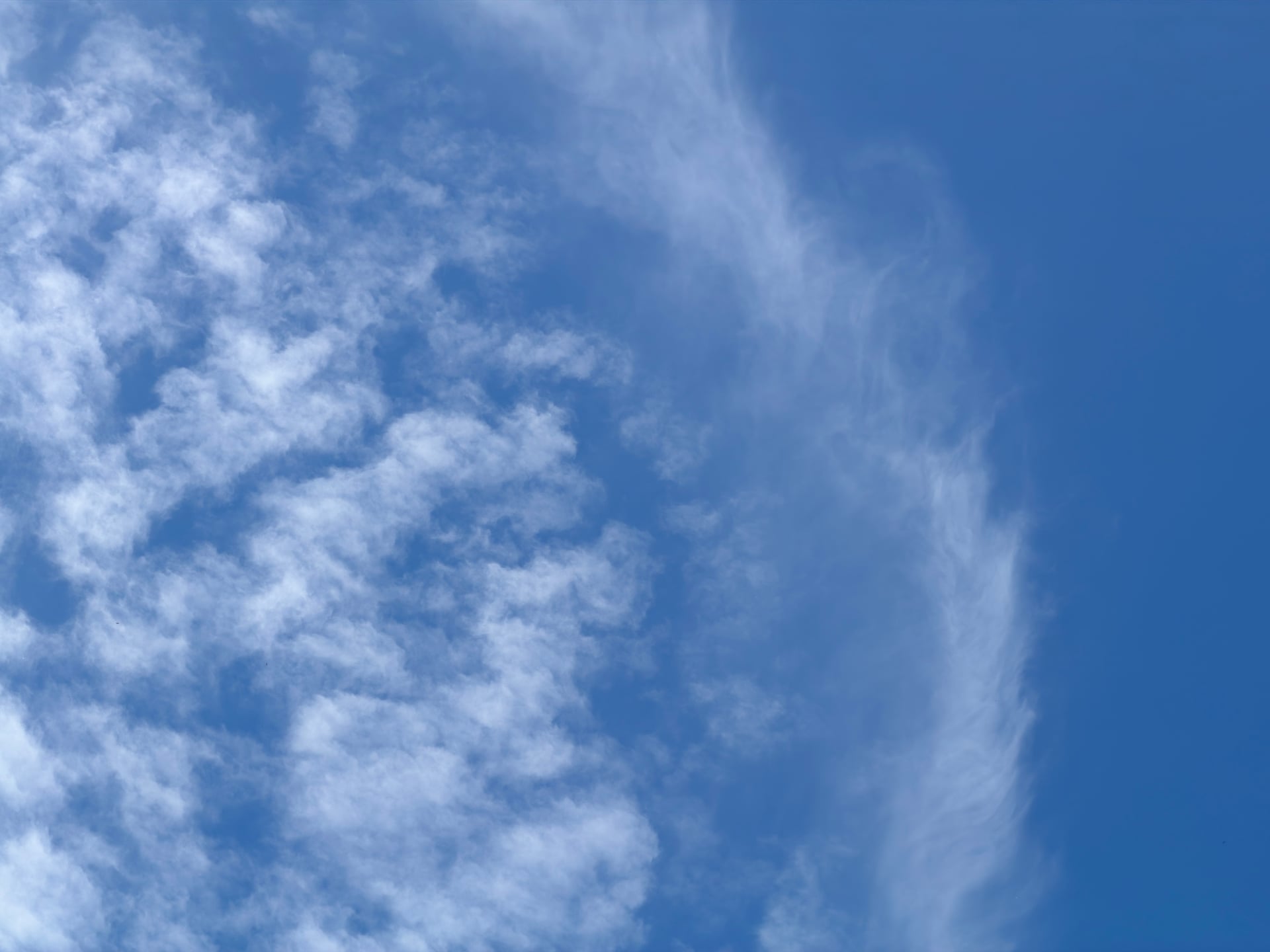 A sweeping band of textured white clouds against blue.